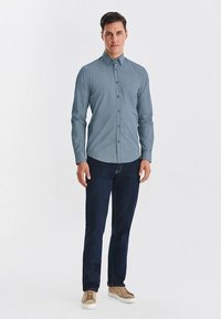 Jasnoniebieska koszula z wzorem, zapinana na guziki, z długimi rękawami, zestawiona z ciemnymi dżinsami i beżowymi trampkami. Koszula ma klasyczny kołnierz i dopasowany krój.