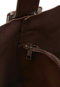 Interno di una borsa a tracolla in pelle marrone con una tasca con zip dotata di hardware argentato. Texture morbida e dettagli di design puliti. C
