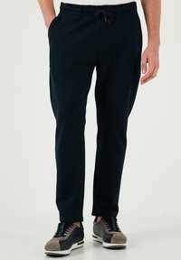 Marineblauwe joggers met elastische tailleband, trekkoord, zijzakken en taps toelopende benen, gemaakt van zachte stof.