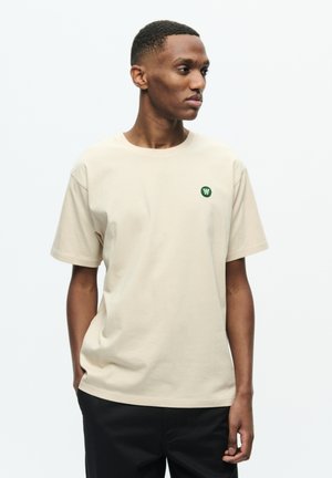 Beige cotton t-shirt with short sleeves, round neckline, and small green logo on the chest; relaxed fit and smooth texture.