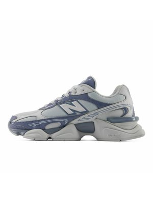 Baskets athlétiques grises et bleues avec une semelle épaisse, tige en mesh et cuir, fermeture à lacets et logo sur le côté.