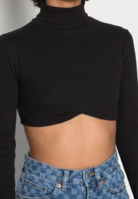 Svart ribbad turtleneck crop top med långa ärmar, med en böjd nederkant. Kombinerad med ljusblå rutig högmidjad jeans.