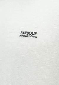 Λευκό ύφασμα με ραβδωτή υφή και μαύρο κεντημένο λογότυπο "BARBOUR INTERNATIONAL" στο μπροστινό μέρος.