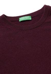 Maglione a maglia borgogna con colletto rotondo a coste. Presenta un'etichetta verde con la scritta "United Colors of Benetton." Texture liscia, spessore medio.