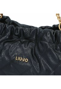 Borsa nera trapuntata con finitura in pelle testurizzata, dotata di un bordo arricciato e accessori in metallo dorato. Nome del marchio "LIU JO" in oro.