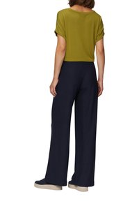 Olivengroene top met korte mouwen in een losse pasvorm, gecombineerd met marineblauwe wijde broek. De broek heeft een geribbelde textuur. Lichte schoenen.