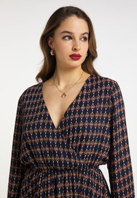 Rochie modelată de culoare bleu marin, cu decolteu adânc în V, mâneci lungi și talie elastică. Materialul are un design floral geometric în nuanțe de roșu și aur.