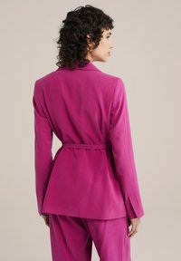 Fuchsie obšitý blazer s úzkým pasem, klopovými límci a dlouhými rukávy. Hladká látka se strukturovaným střihem, zobrazeno zezadu.