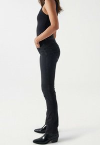 Svarta smala jeans med hög midja, tillverkade av denim. Har en figursydd siluett, diskreta sömmar och två bakfickor. Bärs med svarta klackstövlar.