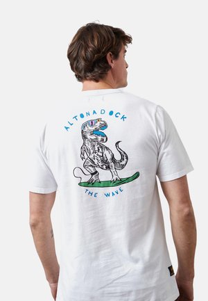 Camiseta de algodón blanca con un gráfico colorido de un dinosaurio en la espalda, un diseño de tabla de surf y un texto que dice "ALTONADOCK THE WAVE".