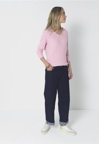 Ljusrosa v-ringad tröja med slim fit och långa ärmar, tillsammans med mörkblå vida jeans som är uppvikta vid fållarna och vita sneakers.