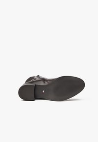 Dunkelbraune Leder-Stiefelette mit runder Zehenform, Blockabsatz, strukturiertem Obermaterial und subtilen Nähdetails. Flache Gummisohle mit Grippatterns.