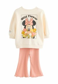 Krämfärgad sweatshirt med en blommig grafik och en prickig rosett, kombinerad med rosa ribbade utsvängda byxor med vågig nederkant.