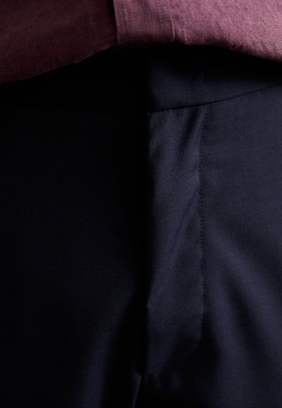 Pantalones oscuros de color navy con una textura suave y un corte recto. La cinturilla está oculta bajo una camisa burdeos, visible parcialmente por encima.