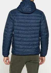 Giacca a vento blu navy con cuciture orizzontali, cappuccio e polsini elasticizzati. Realizzata in un materiale leggero e liscio, presenta un design aderente.