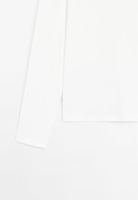 Hvid skjorte med lange ærmer, glat tekstur og løs pasform. Skjørtet er lige, og ærmekanterne har en enkel, afrundet finish.