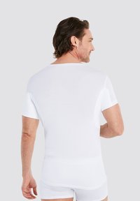 White short-sleeve shirt made of smooth fabric, featuring a crew neck and a relaxed fit. Visible seams and a clean, simple design.
