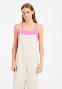 Pantalones de tirantes beige con un ajuste relajado y correas ajustables, combinados con una camiseta de tirantes ajustada de color rosa. Tejido suave con un hardware mínimo.