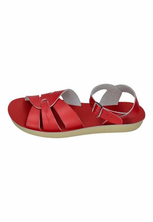 Red flat sandal with crisscross leather straps, ankle strap with metal buckle, and beige rubber sole.