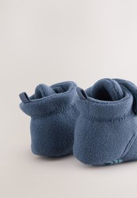 Chaussons en polaire bleue avec un design à revers roulé, une texture douce et une semelle antidérapante texturée présentant un motif subtil.