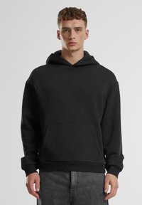 Schwarzer Kapuzenpullover aus weichem Stoff, mit einer vorderen Tasche und gerippten Bündchen. Das Design ist locker und minimalistisch.