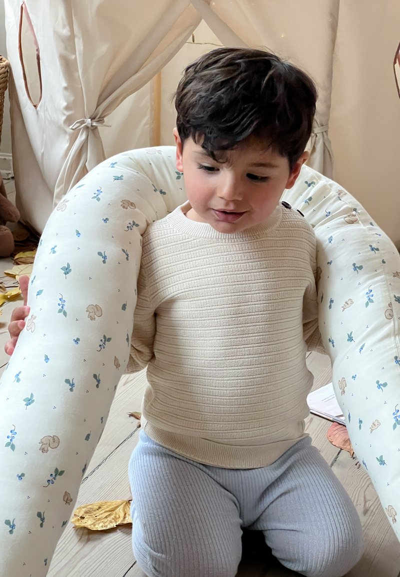 Μαλακό μαξιλάρι θηλασμού από βαμβάκι με floral και ζωγραφισμένες λεπτομέρειες. Παιδί με ανοιχτό μπεζ υφασμάτινο πουλόβερ και ανοιχτό μπλε πάνες με ραβδώσεις.