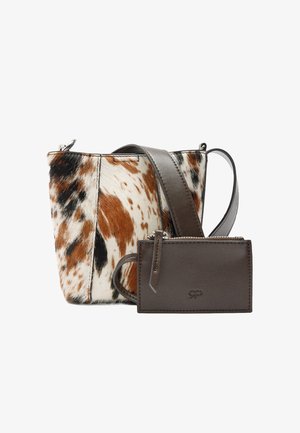 Mała torba typu bucket z wzorem skóry krowy w kolorach brązowym, czarnym i białym, szeroki, ciemnobrązowy pasek skórzany oraz dopasowana ciemnobrązowa saszetka na suwak.