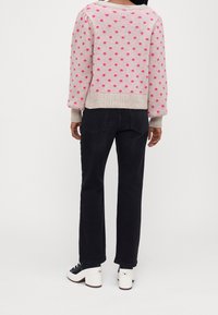 Jersey de punto en rosa claro con lunares rosas contrastantes, combinado con jeans negros y zapatos de tacón cuadrado blancos.