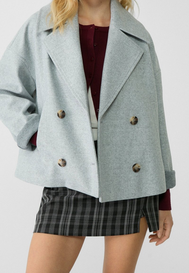 Veste gris clair croisée en mélange de laine avec revers crantés et boutons en écaille, associée à une mini-jupe écossaise noire et grise.