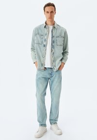 Vaatevalikoima sisältää vaaleansinisen farkkutakin, jossa on kaksi suurta rintataskua, ja yhdistelee sitä sopiviin vaaleansinisiin farkkuihin. Mallilla on päällään valkoinen T-paita ja valkoiset lenkkarit.