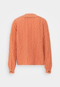 Orange, tekstureret jakke med lange ærmer, der har et quiltet design og et sort prikket mønster. Knaplukning ved ærmeenderne.