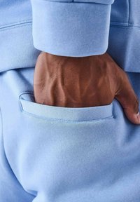 Lichtblauwe sweatshirtstof met een textuurafwerking, met een zichtbare hand in een zijzak en een manchet aan de mouw.