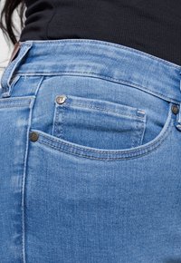 Lichtblauwe denim jeans in een klassieke vijf-pocket stijl, met een achterzak met metalen klinknagels en contrasterende stiksels.