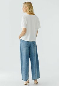 Witte top met korte mouwen en een ontspannen pasvorm, gecombineerd met lichte spijkerbroek met wijde pijpen. De jeans hebben achterzakken en een vervaagde afwerking.