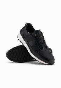 Le scarpe sportive nere presentano una combinazione di pelle liscia e rete testurizzata, una intersuola bianca e una suola in gomma con un motivo a zigzag.