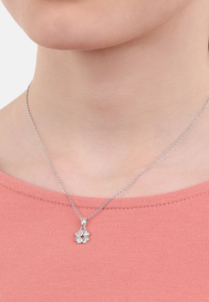 Collana con pendente d'argento caratterizzata da un design floreale con una piccola gemma di accento, appesa a una delicata catena, indossata su una maglietta rosa.