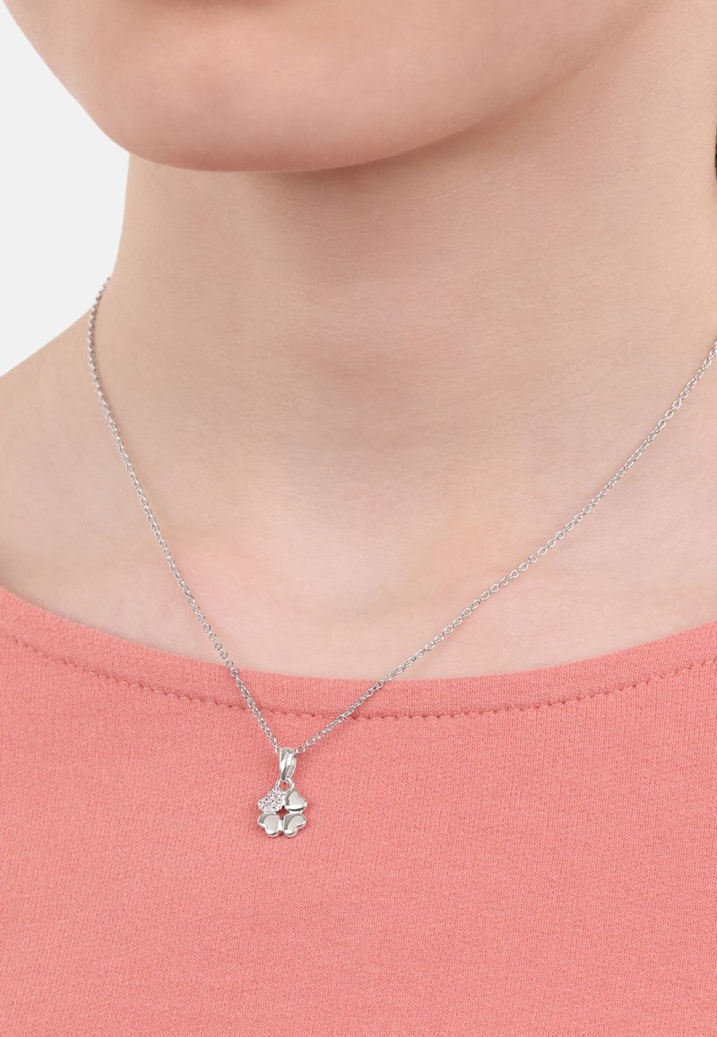 Collana con pendente d'argento caratterizzata da un design floreale con una piccola gemma di accento, appesa a una delicata catena, indossata su una maglietta rosa.