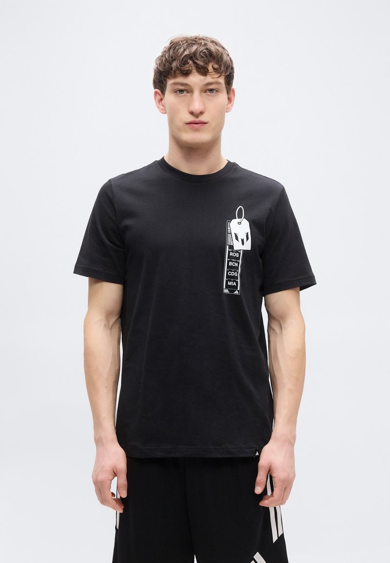 Μαύρο βαμβακερό t-shirt με εκτυπωμένο γραφικό από ετικέτες αποσκευών με κείμενα στην αριστερή πλευρά. Κοντά μανίκια και στρογγυλή λαιμόκοψη.