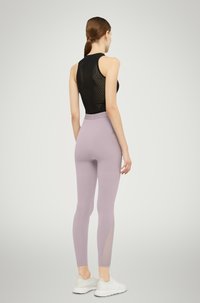 Top nero senza maniche, leggings viola con dettagli in mesh, e scarpe bianche. Tessuto liscio, design aderente e cintura elastica.