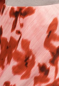 Rosa Stoff mit unscharfem rotem Blumenmuster und feiner diagonaler Textur, vor einem grauen gerippten Hintergrund gezeigt.