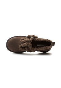 Scarpa in suede marrone con suola nera spessa, rivestimento morbido all'interno e una cintura con fibbia sopra, vista dall'alto su uno sfondo bianco.
