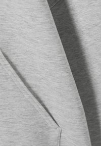 Tessuto morbido grigio chiaro con cuciture visibili e una cucitura ripiegata, che mette in risalto la texture e i dettagli del materiale.