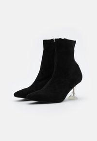 Botines de ante negros con punta afilada y un tacón triangular transparente. Cierre de cremallera, textura suave y diseño ajustado.