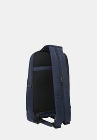 Mochila bandolera azul marino con panel trasero acolchado de malla negra, correa ajustable y cierre visible con cremallera en la correa.