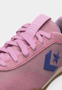 Κοντινό πλάνο ροζ σουέντ αθλητικού παπουτσιού με ροζ κορδόνια, μπλε αστέρι και λογότυπο κεβρόν, και την επιγραφή "All Star" χαραγμένη στην ετικέτα της γλώσσας.