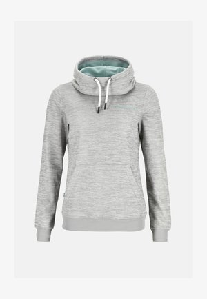 Kobieta stoi z rękami w kieszeniach, ubrana w dopasowany jasnoszary hoodie i dresy, z białymi sneakersami na białym tle.