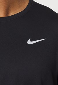 Czarny sportowy t-shirt wykonany z teksturowanej tkaniny, z małym białym logo Nike na górnej lewej części klatki piersiowej, okrągły dekolt.