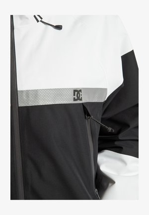 Czarno-biała kurtka z błyszczącym srebrnym pasem i logo DC. Posiada zamek błyskawiczny oraz regulowany sznurek przy kołnierzu.