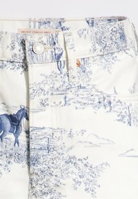 Denim blanco con estampado de paisaje azul, con un corte recto hasta el tobillo, cierre frontal con botón y sutiles acentos en cobre.