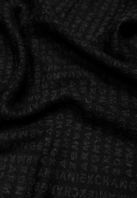 Tessuto nero caratterizzato da un sottile motivo ripetuto di lettere. Il materiale è morbido con una leggera texture, creando un aspetto stratificato.